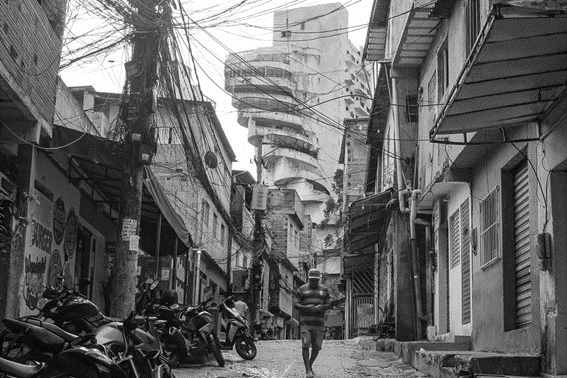 Fotografia em preto e branco de uma rua estreita da favela de Paraisopolis, na zona sul de Sao Paulo, com o edificio de luxo Penthouse ao fundo